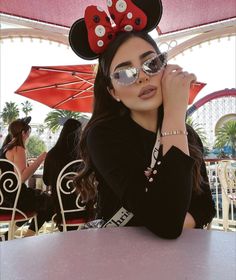 a woman sitting at a table with minnie mouse ears on her head and sunglasses over her eyes