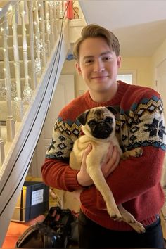 a man holding a small pug in his arms while standing next to a stair case