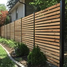 a wooden fence in front of a house with grass and bushes on the side walk