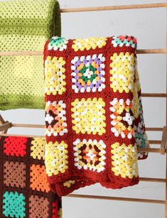 two crocheted blankets are hanging on a clothes rack, one is red and the other is green