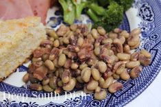 a blue and white plate topped with beans and broccoli next to ham on a piece of bread