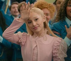 a woman in a pink dress is surrounded by other people and waving her hands up