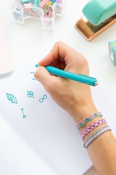 a person writing on a piece of paper with a pen in their hand and other office supplies around them