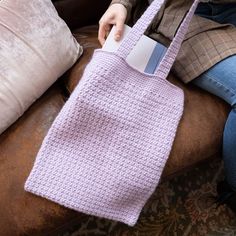 a woman sitting on a couch holding a pink crocheted bag with a tag in it