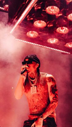 a man standing on top of a stage holding a microphone in his hand and wearing a hat