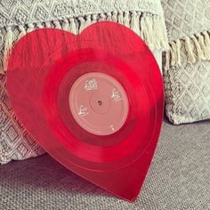 a red heart shaped vinyl record sitting on top of a couch next to a pillow