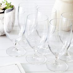 several empty wine glasses are lined up on a white tablecloth with a vase in the background