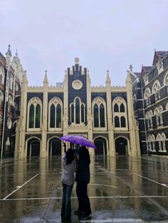 two people standing under an umbrella in front of a large building on a rainy day