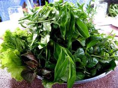 a metal bowl filled with lots of green leafy vegetables on top of a table