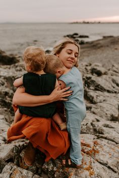 a woman holding a child on top of rocks near the ocean