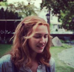 a woman with red hair is looking down at her cell phone while standing in the grass