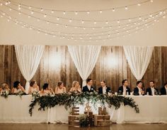 a group of people sitting at a table in front of white drapes and lights