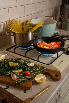 two pans with food cooking on top of a stove next to cutting boards and utensils