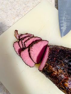 a piece of meat sitting on top of a white cutting board next to a knife