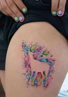 a woman's thigh with an unicorn tattoo on the side and colorful paint splatters all over it