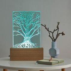 a table with a book, vase and tree laser cut lamp on top of it