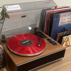 a red record player sitting on top of a wooden table next to books and cds