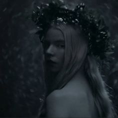 a woman with long hair wearing a wreath of flowers on her head in the woods