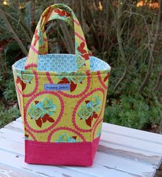 a colorful bag sitting on top of a wooden table next to bushes and trees in the background