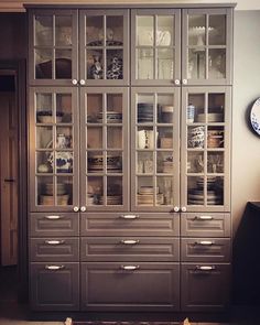 a cabinet with glass doors and drawers in a living room next to a clock on the wall