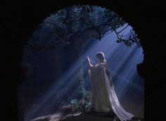 a woman dressed in white is holding her hand up to the light coming from behind