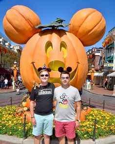 two men standing next to each other in front of a mickey mouse pumpkin head statue