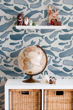 a globe sits on top of a white cabinet in front of a blue and white wallpaper