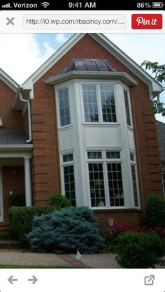 a red brick house with white trim on the front and side windows, bushes and shrubs