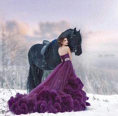 a woman in a long purple dress standing next to a horse on snow covered ground