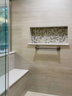 a bathroom with a glass shower door and tiled walls, along with a white bench