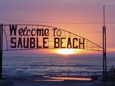 a welcome to sauble beach sign at sunset with the ocean in the background