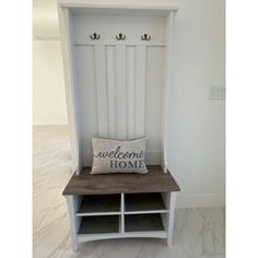 an entryway bench with a welcome home pillow on the top and two coat racks above it