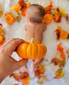 a person holding a small pumpkin in front of a baby