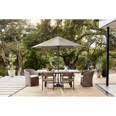 an outdoor table with chairs and umbrellas on the outside decking area in front of some trees