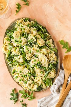 a plate full of pasta and vegetables next to a wooden spoon on a pink surface