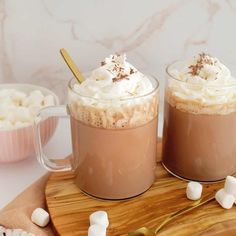 two mugs filled with hot chocolate and marshmallows on a cutting board