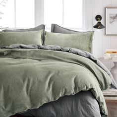 a bed with green sheets and pillows next to a white table in front of a window