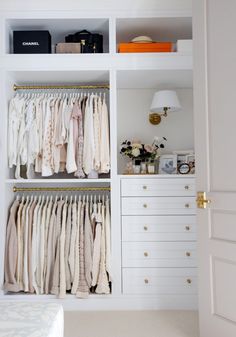 an open closet with clothes hanging on hangers and drawers in the corner, next to a bed