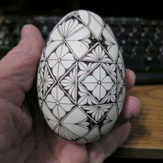 a hand holding an egg with designs painted on it in front of a computer keyboard