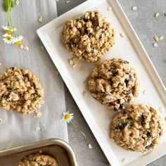 three oatmeal cookies sitting on top of a white plate next to a cookie tin