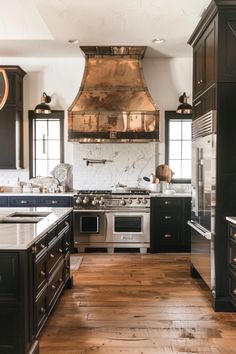 a large kitchen with wooden floors and black cabinets, stainless steel range hood over the stove