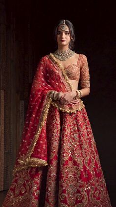 a woman in a red and gold bridal gown standing with her hands on her hips