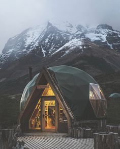 a small wooden cabin in the mountains with snow on the mountain behind it and lights at the entrance