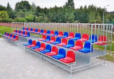 rows of blue and red chairs sitting on top of a brick floor next to a fence