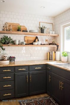 a kitchen with black cabinets and white subway backsplash, wooden shelves above the sink