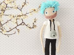 a crocheted doll standing next to a branch with white flowers in the background