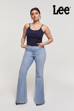 Woman standing in front of a white background. She is standing on her left leg with her right knee bent. She has her hands in her pockets and is looking confidently at the camera. She is wearing a navy blue Lee tank top and light blue denim flare jeans. Dressing Casual, Style Flare Jeans, Casual Night Out