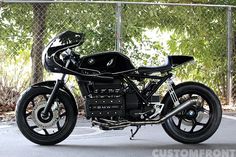 a black motorcycle parked on top of a parking lot next to a fence with trees in the background