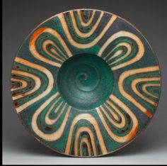 a green and brown bowl with swirl designs on it's side, sitting on a table