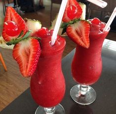 two glasses filled with strawberries and juice on top of a table